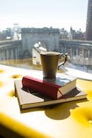Vista da janela mostrando uma ponte, edifícios, uma xícara e um livro sobre uma superfície amarela.