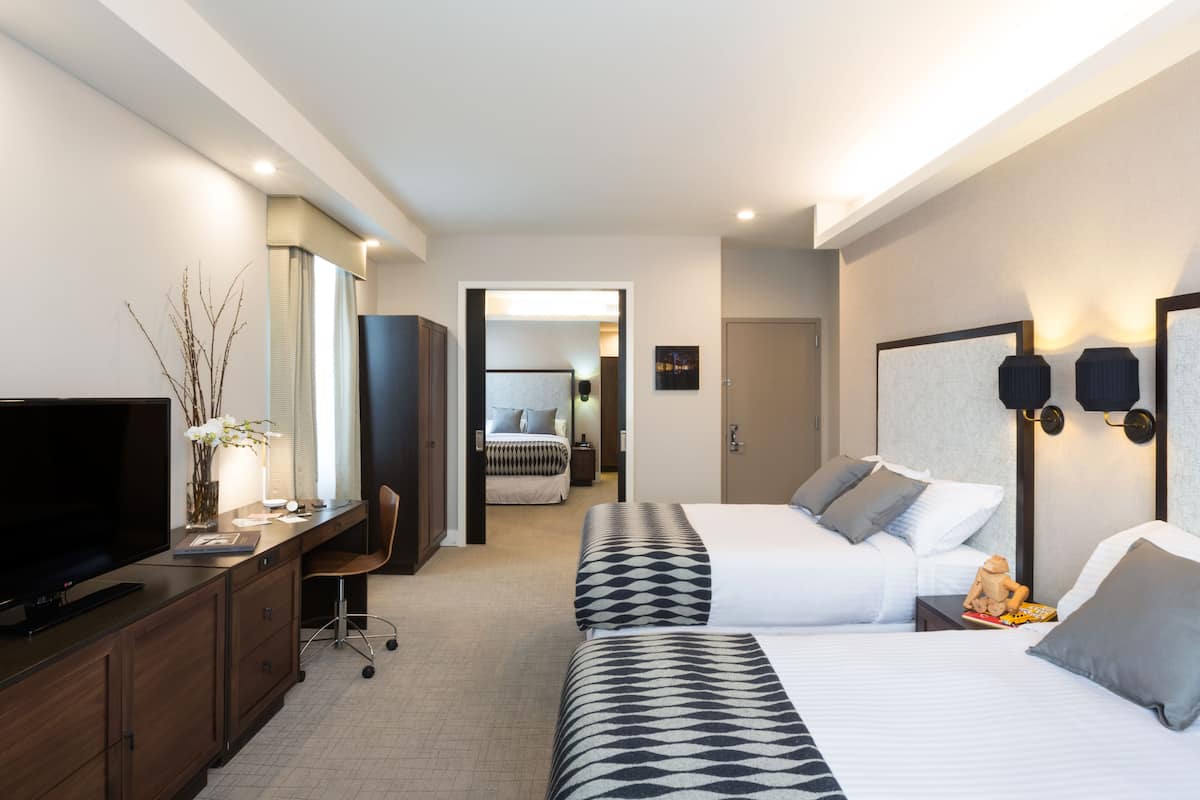 A hotel room with a desk, TV, two beds, and a bathroom visible through an open door.