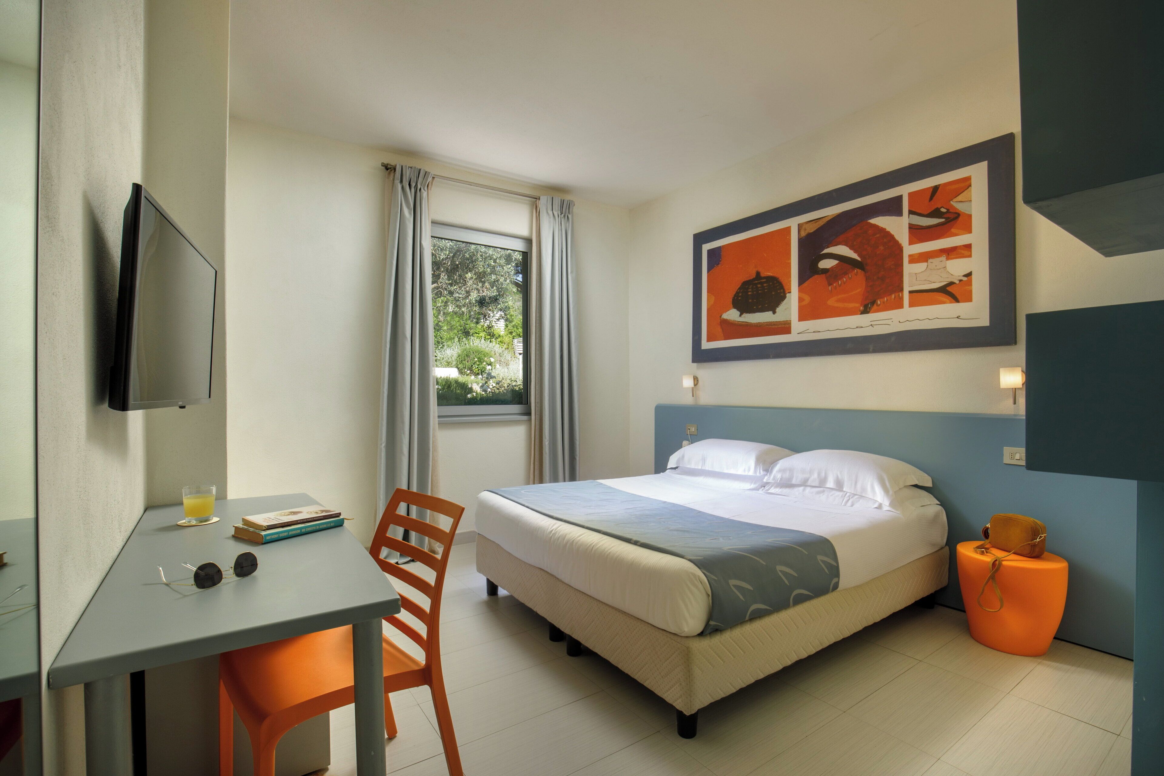 A hotel room with a bed, a desk, a chair, a TV, and a window with curtains.