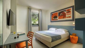 A hotel room with a bed, a desk, a chair, a TV, and a window with curtains.