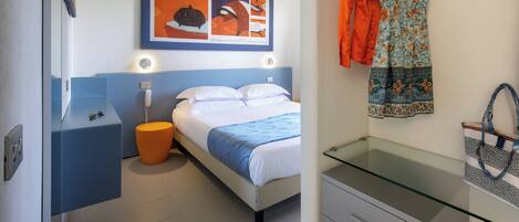 Una moderna camera d'hotel con un letto, un comodino, una scrivania con piano in vetro e un'opera d'arte appesa al muro.