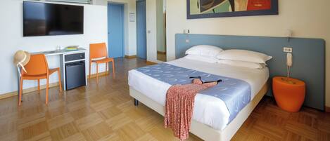 A hotel room with a bed, desk, chairs, a television, and a painting on the wall.