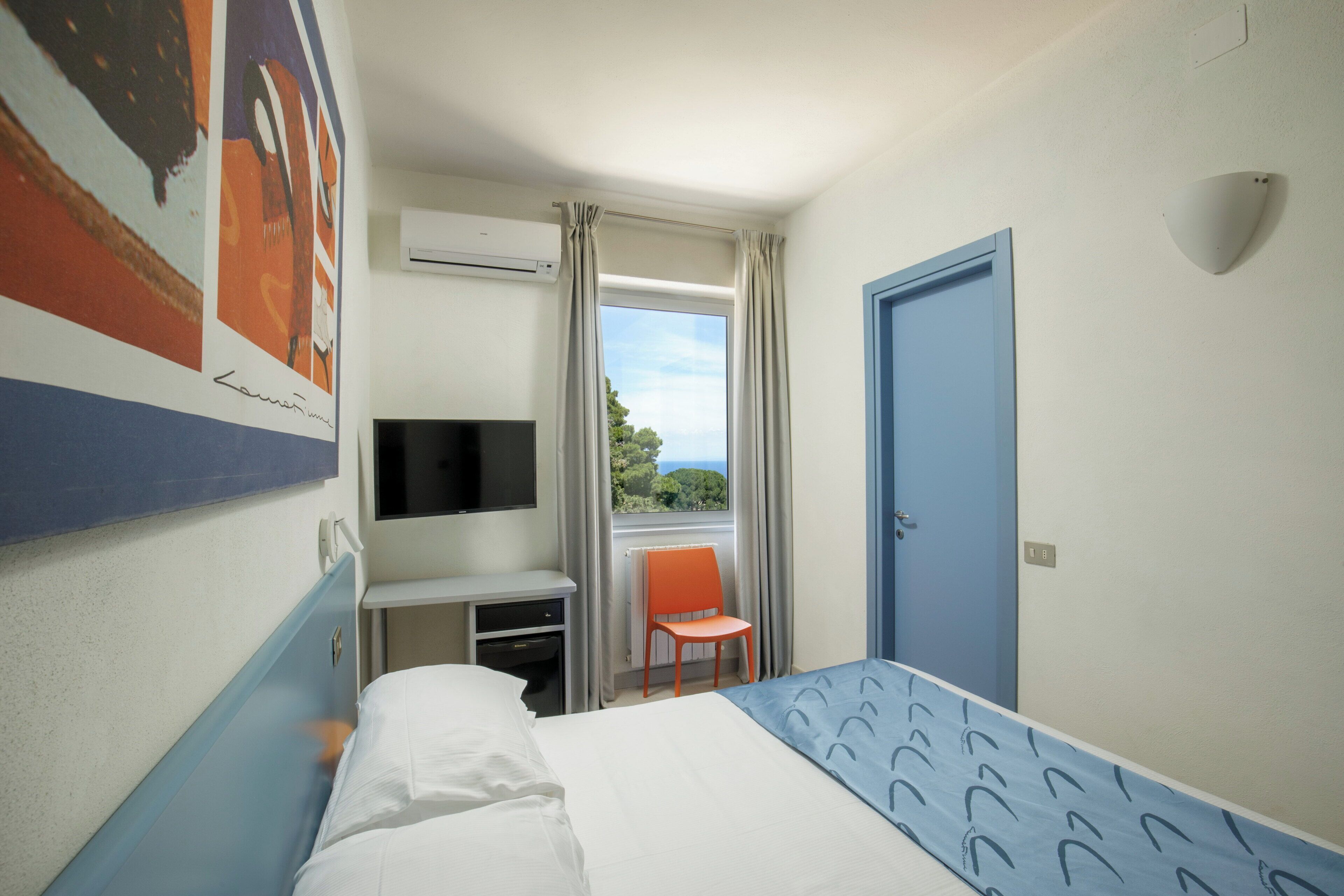 Ein Hotelzimmer mit einem Bett, einem Schreibtisch, einem Flachbildfernseher, einem Stuhl und einem Fenster mit Vorhängen.