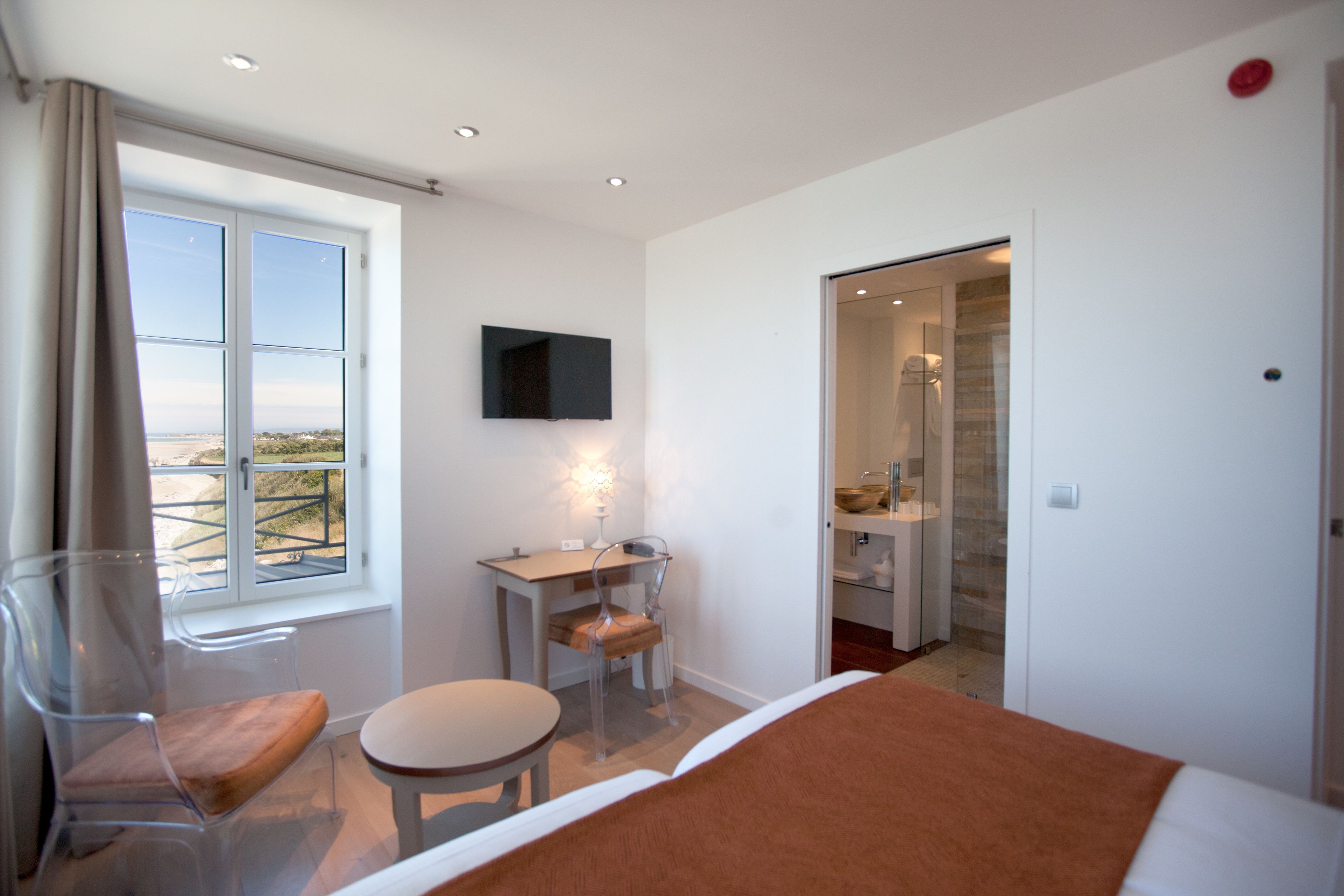 A bedroom with a bed, a desk, a chair, a TV, and a bathroom visible through an open door.