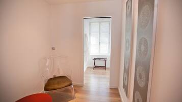 Um quarto com uma cadeira transparente, um banco de madeira e uma porta que dá para outro cômodo.