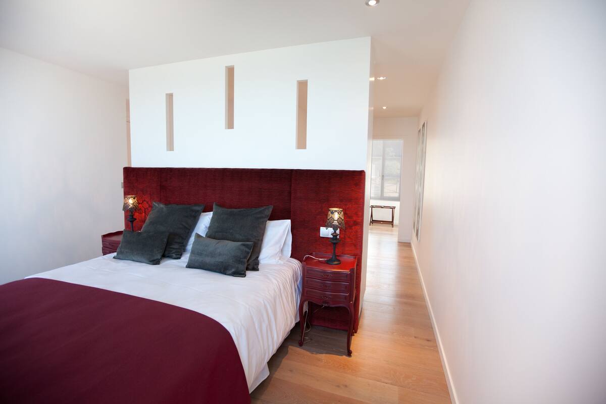A modern bedroom with a large bed, two bedside tables, and a red headboard.