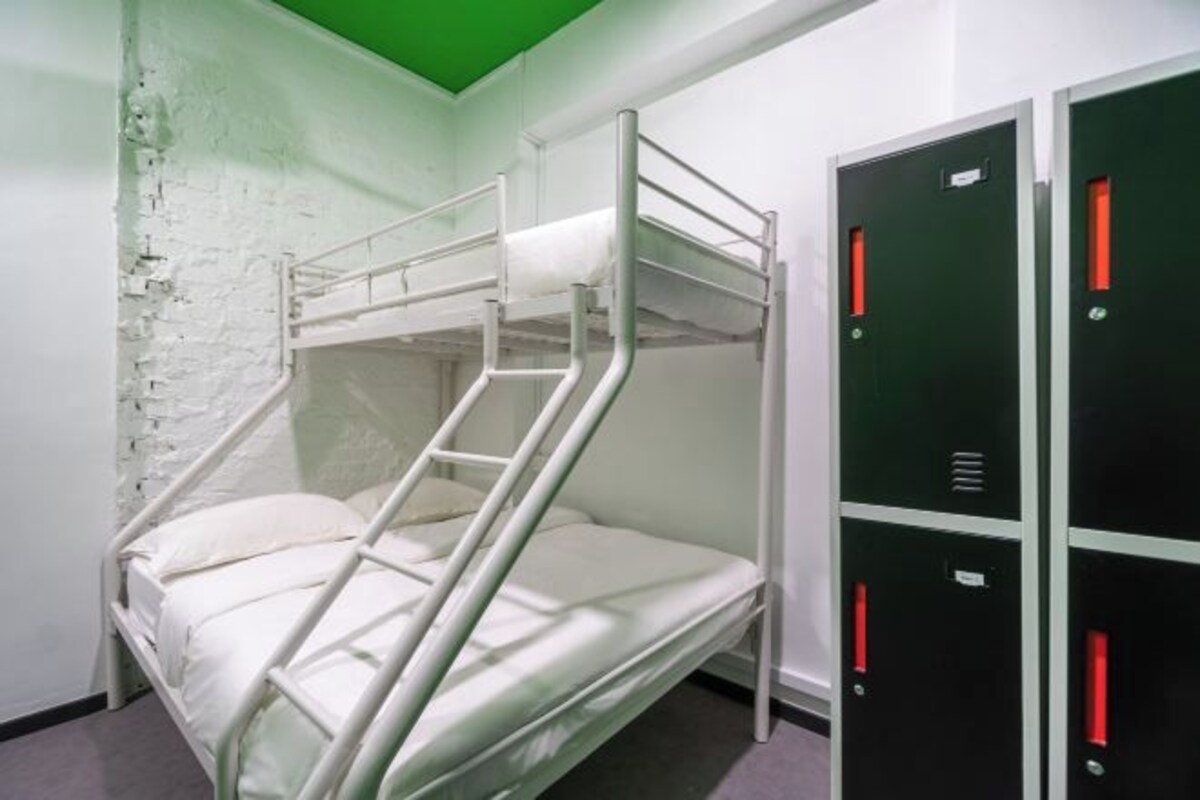 A bunk bed with a ladder, a white brick wall, and a set of black lockers with red handles.
