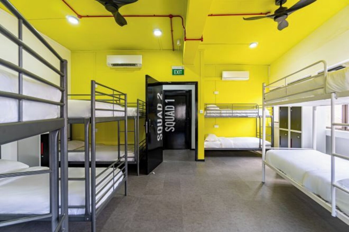 A dormitory room with bunk beds, an exit sign, and a door labeled "SQUAD 1".