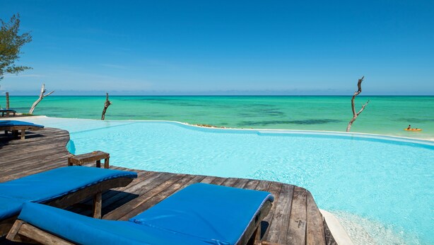 Una terraza de madera con sillones de descanso y una piscina con vistas a aguas turquesas.