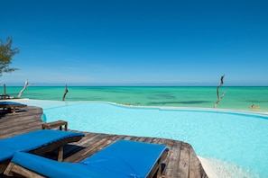 Um deck de madeira com cadeiras de descanso e piscina com vista para águas azul-turquesa.