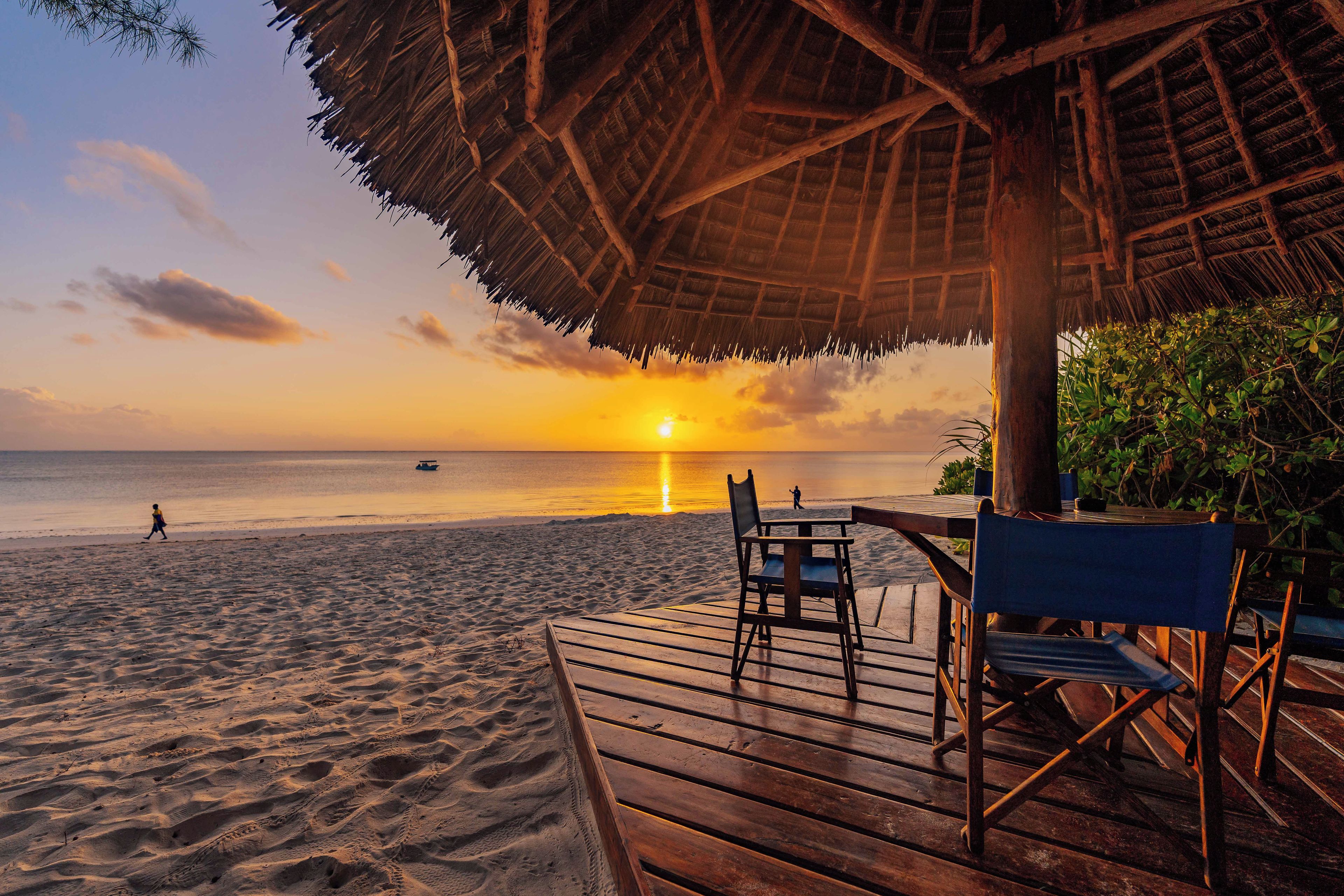 Una terraza de madera con sillas que da vista a una playa al atardecer.