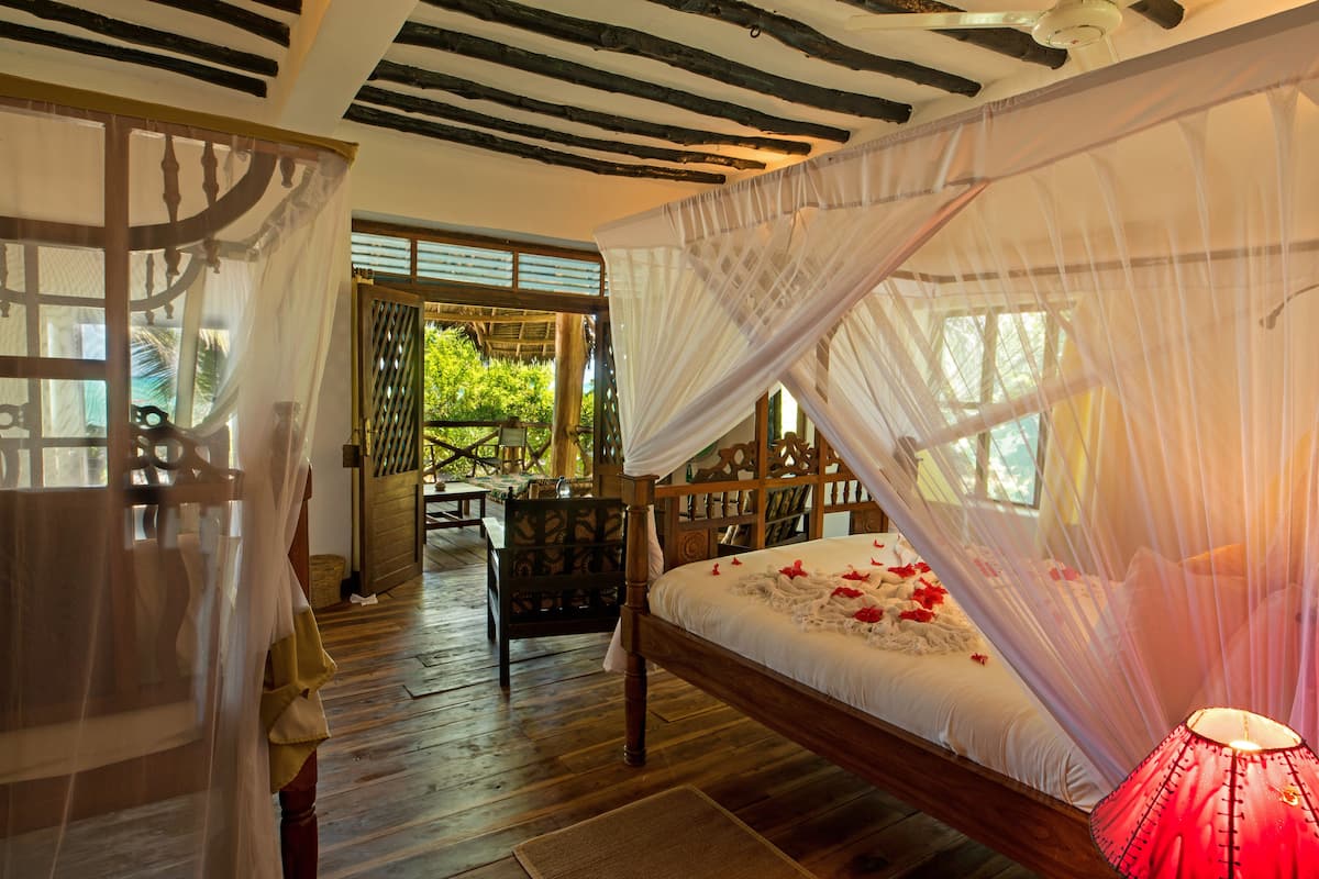 Una habitación con cama bajo un dosel, muebles de madera y vistas al exterior con vegetación.