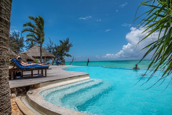 Relax by the serene pool surrounded by thatched-roof structures and lounge chairs.