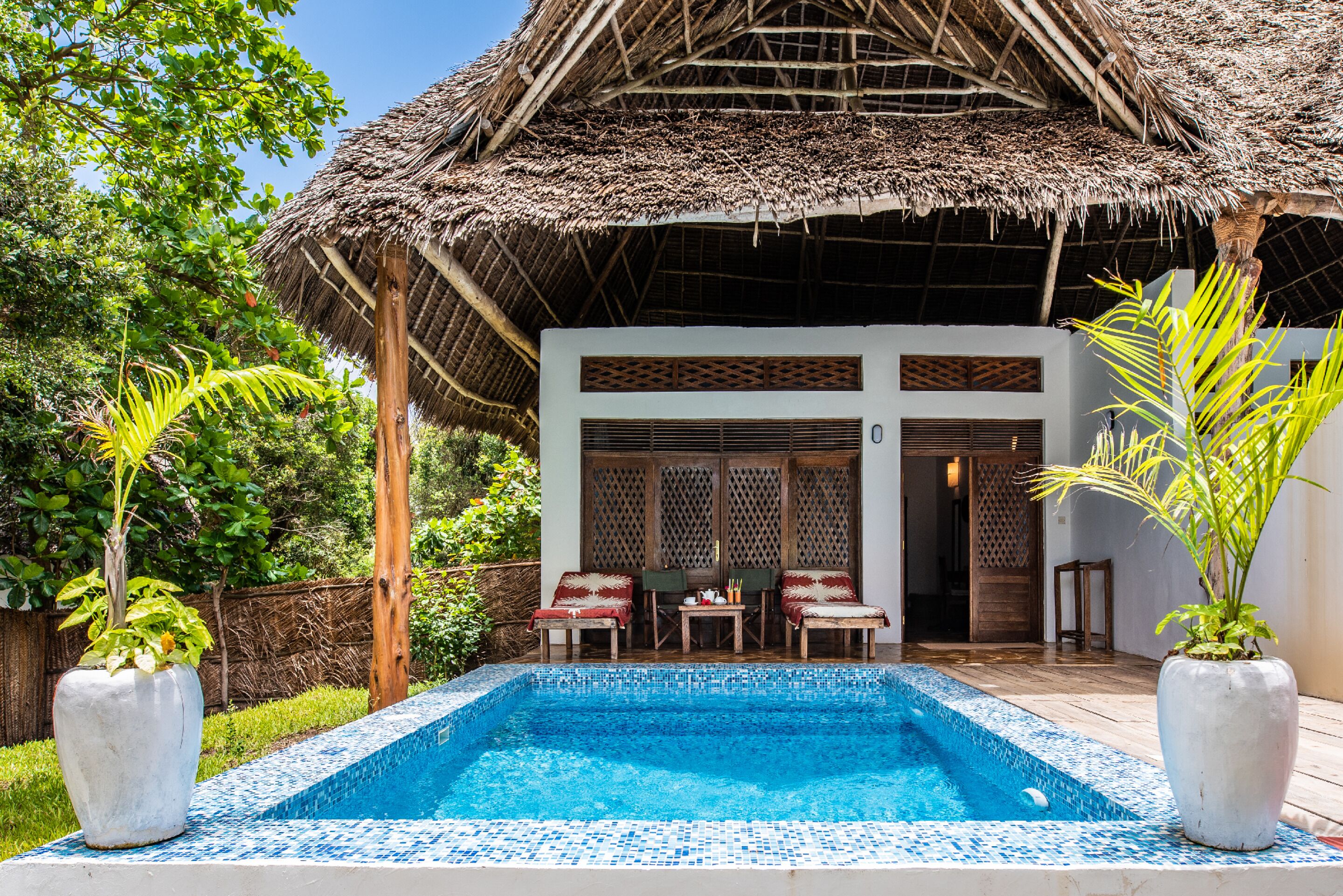 A pool area with a thatched-roof structure, two chairs, and a table.