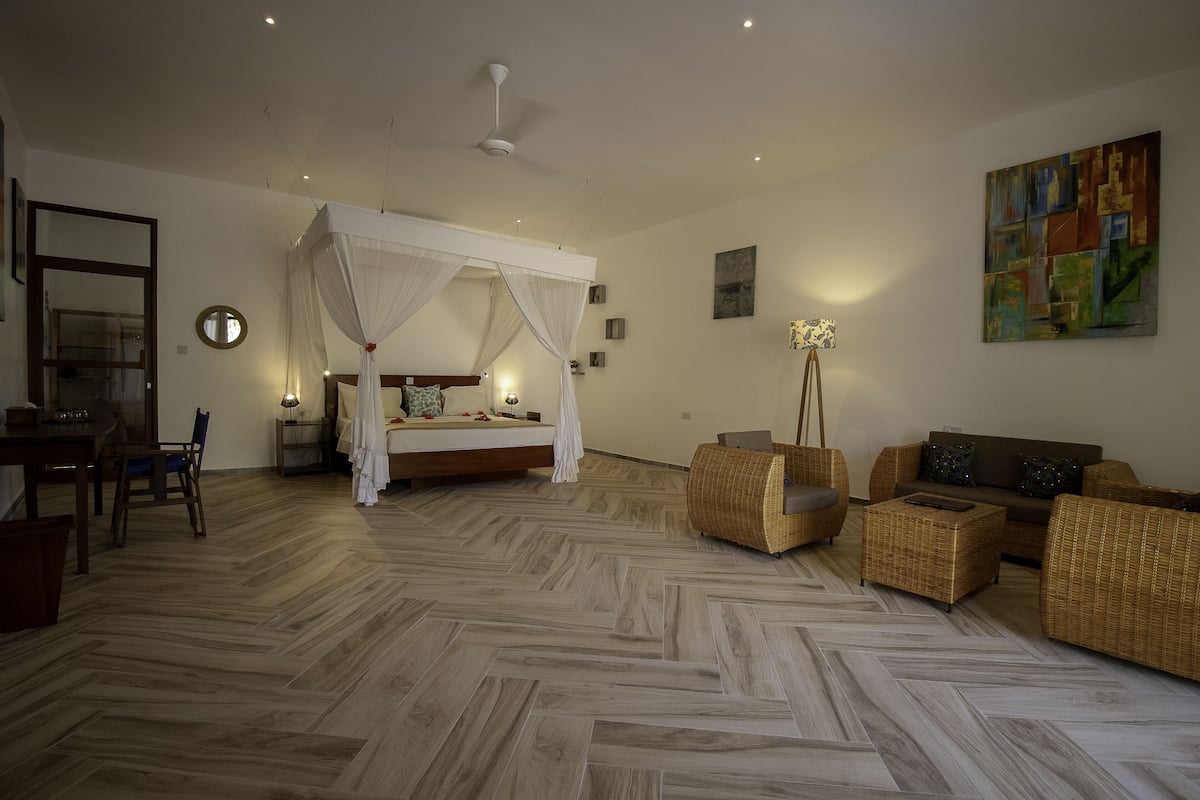Un dormitorio con cama con dosel, un sofá, mobiliario de mimbre y un suelo con patrón de espiga.