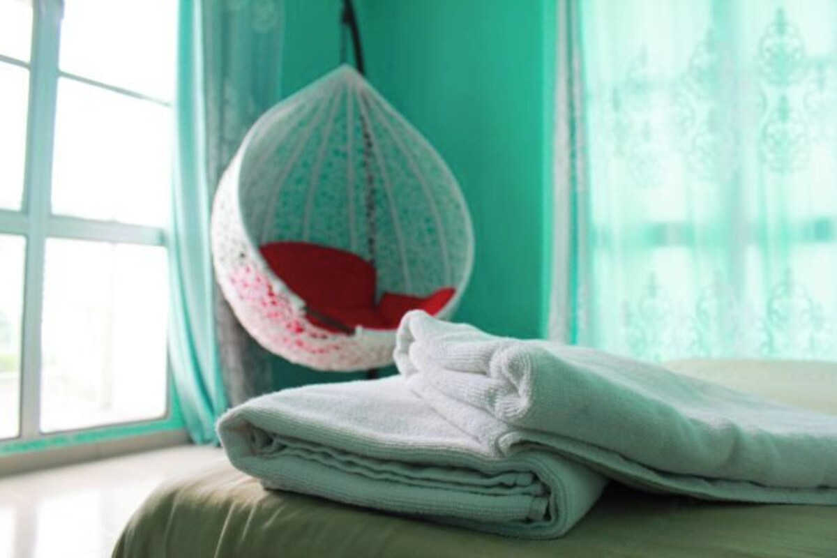 A neatly folded white towel on a bed with a hanging chair in the background.