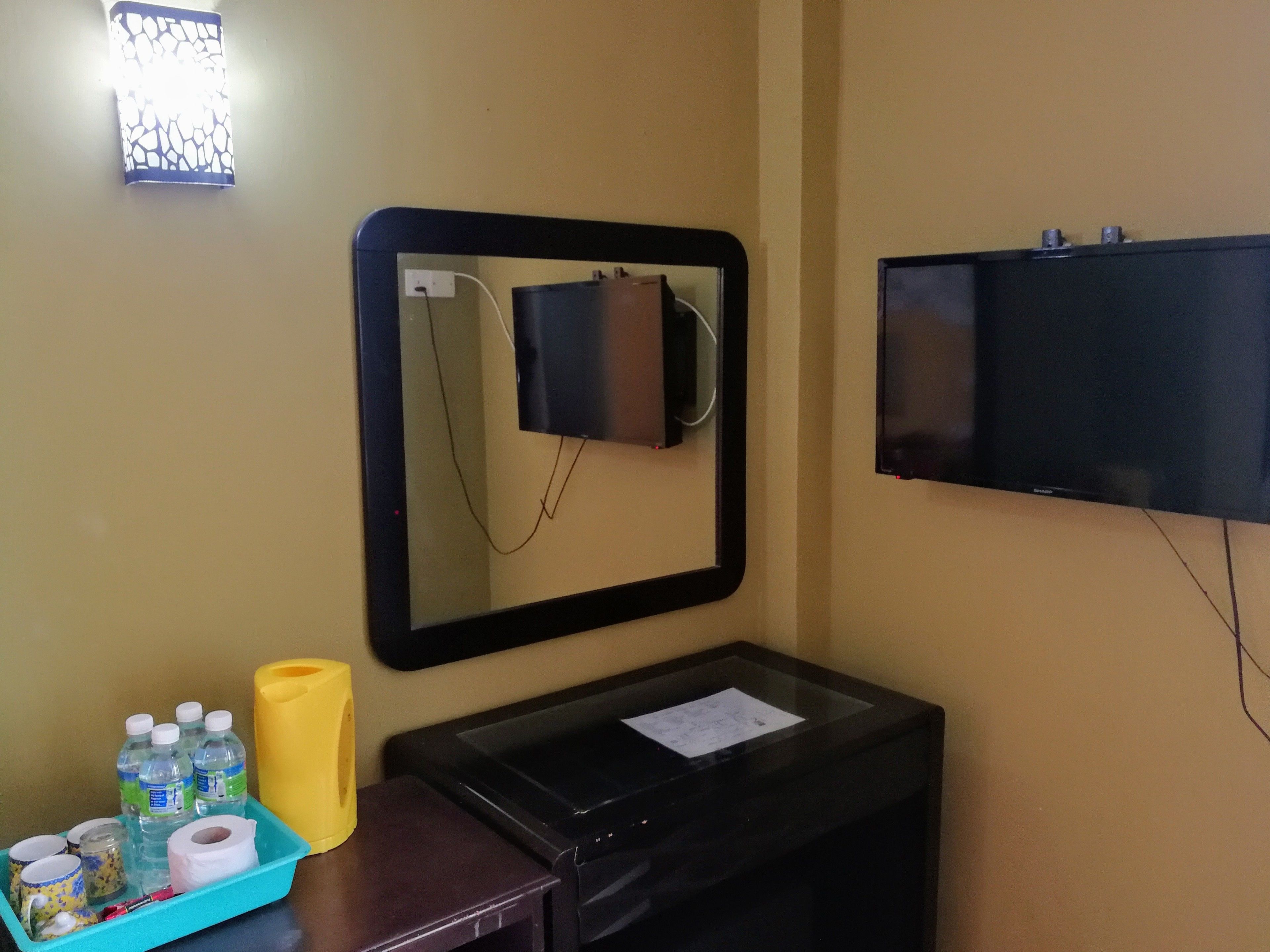 A hotel room with a large mirror, a flat-screen TV, a desk with a paper, and a tray with toiletries.