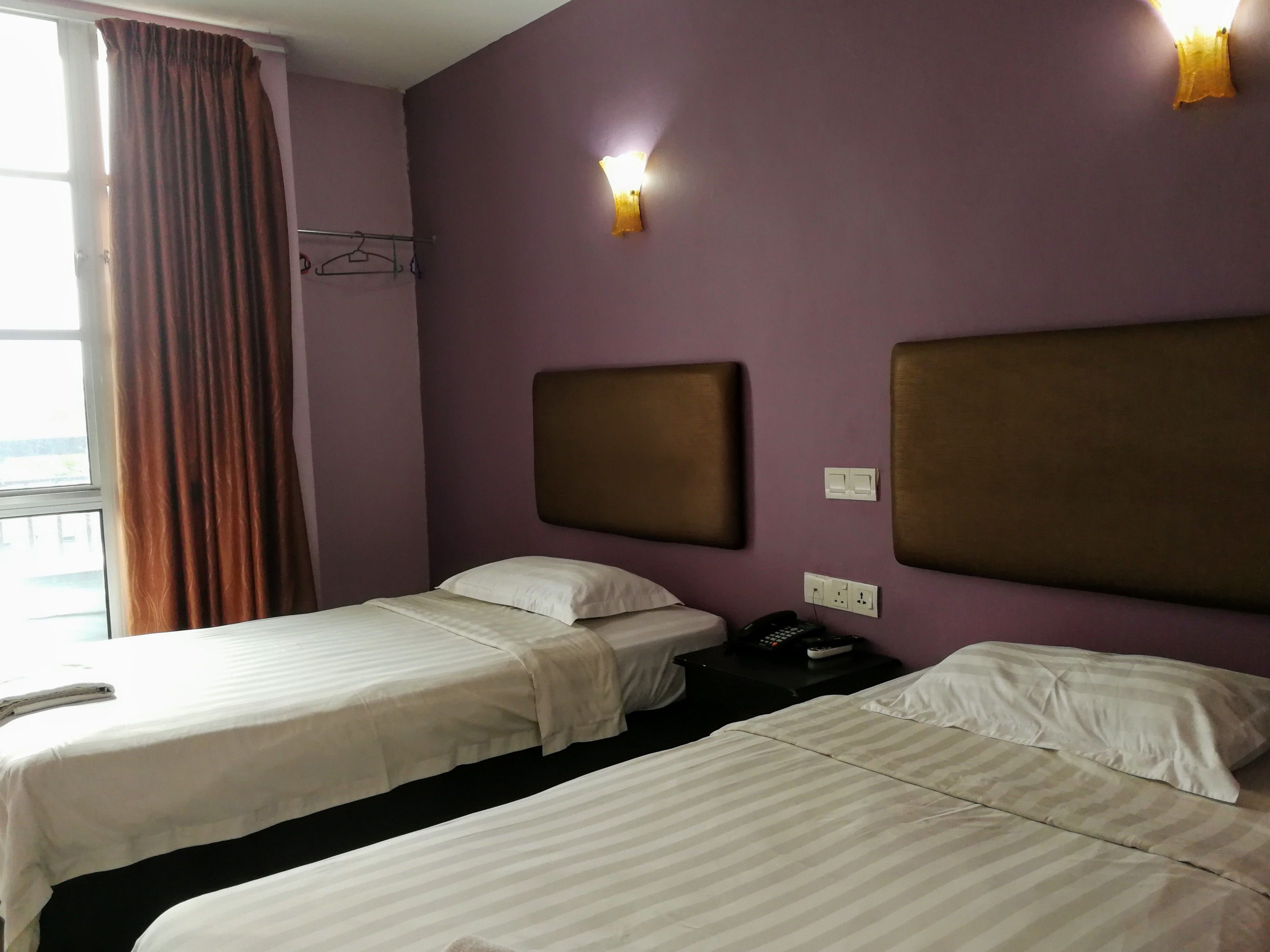 Une chambre d’hôtel avec deux lits, une fenêtre avec des rideaux, une table de chevet avec un téléphone et des lampes fixées au mur.