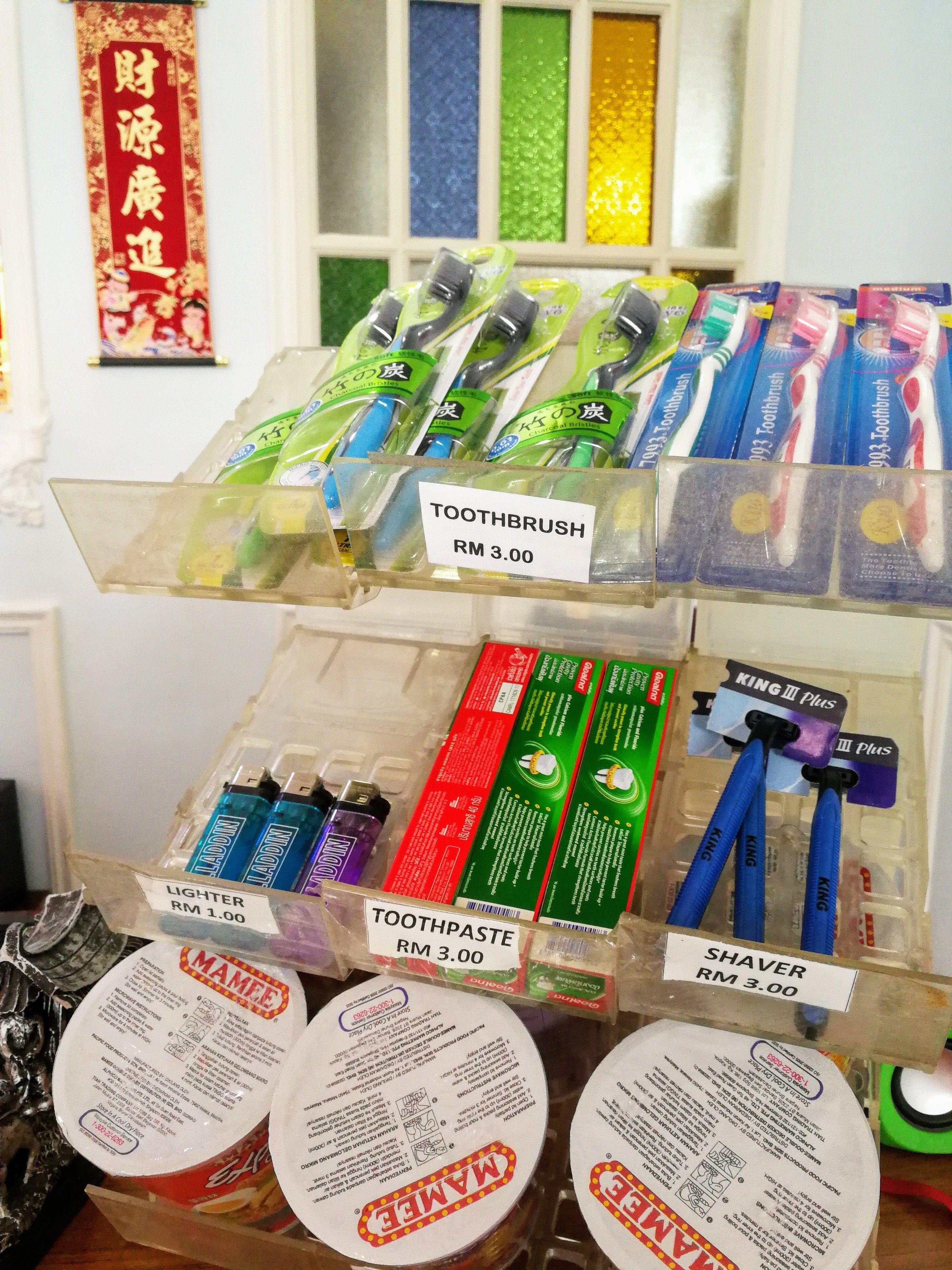 Exhibición de productos para higiene bucal, incluyendo cepillos de dientes, pasta dental y afeitadoras, con etiquetas de precio.