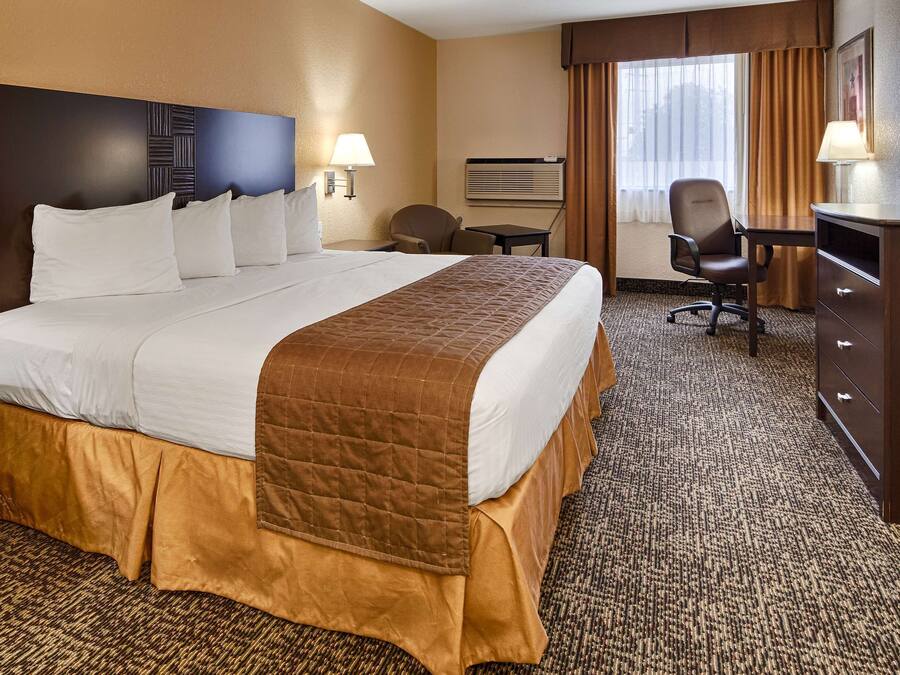 A hotel room with a large bed, a desk, a chair, a TV, and a window with curtains.