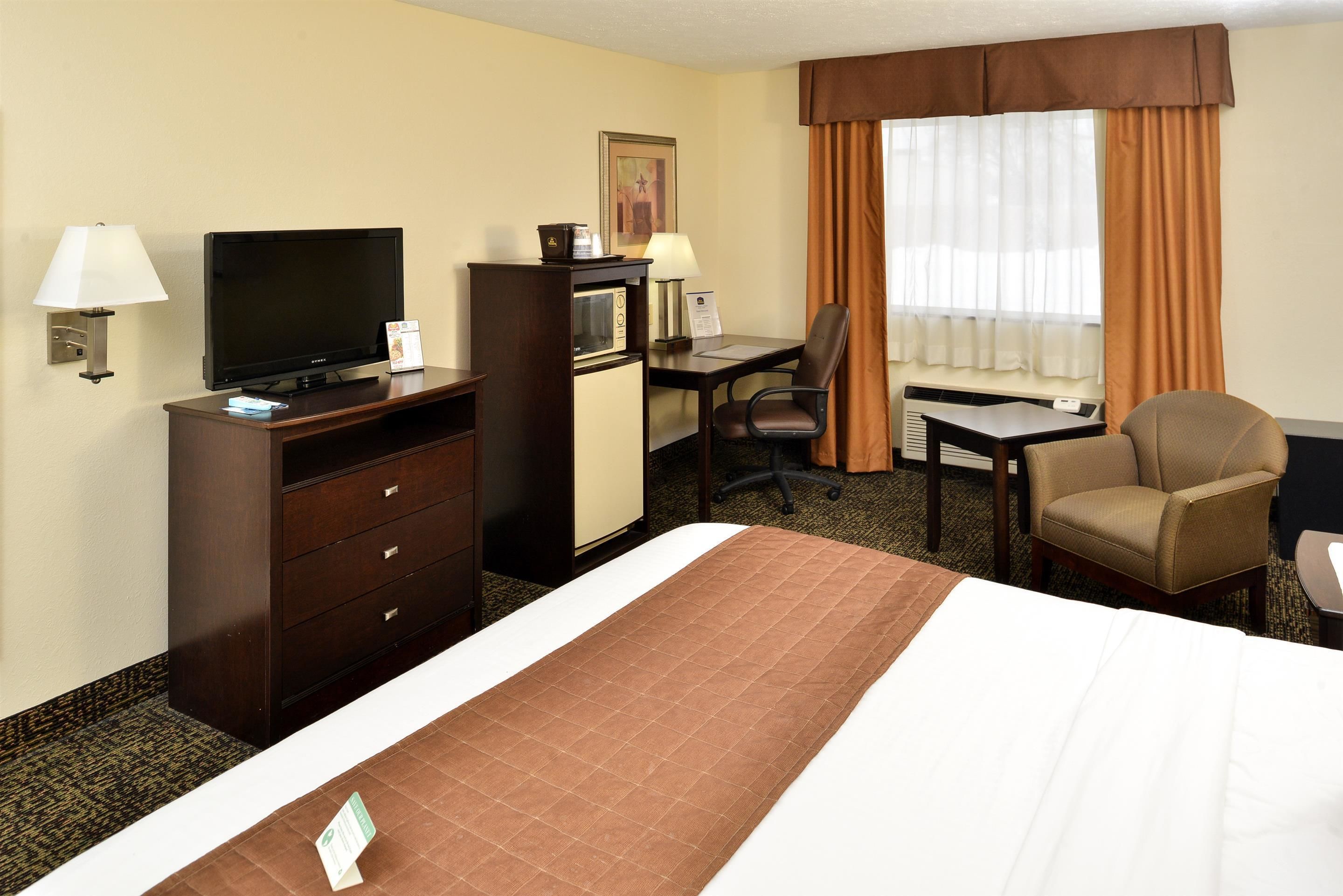 A hotel room with a bed, a desk with a chair, a television, a microwave, and a lamp.