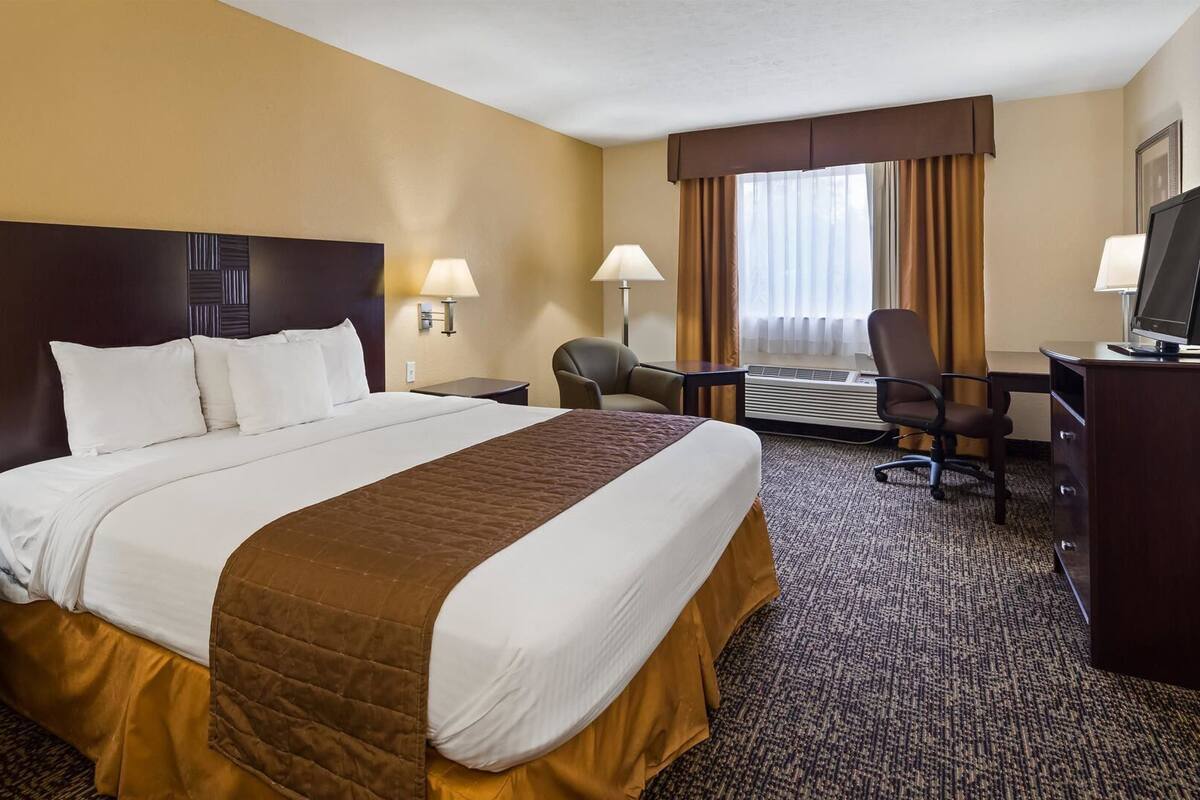 A hotel room with a large bed, two bedside tables, a desk with a chair, a TV, and a window with curtains.