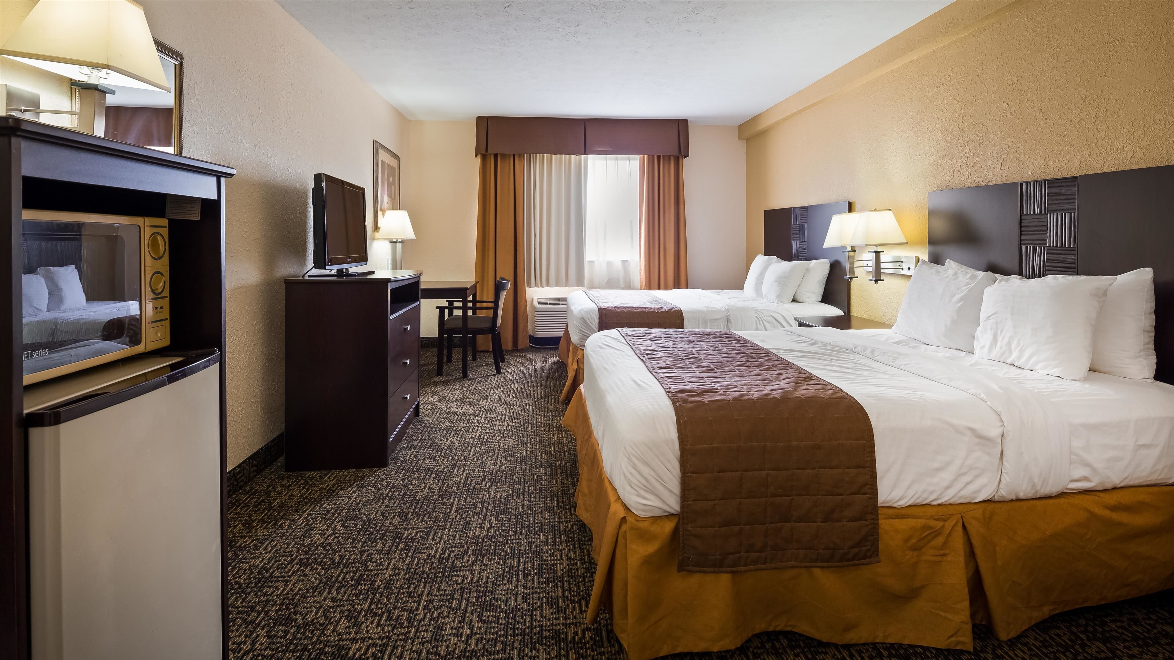 A hotel room with two beds, a desk with a television, a chair, and a minibar.