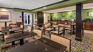A hotel lobby with a dining area featuring tables and chairs, a kitchen area with appliances, and a green wall with various signs. - Best Western Inn (Elyria)