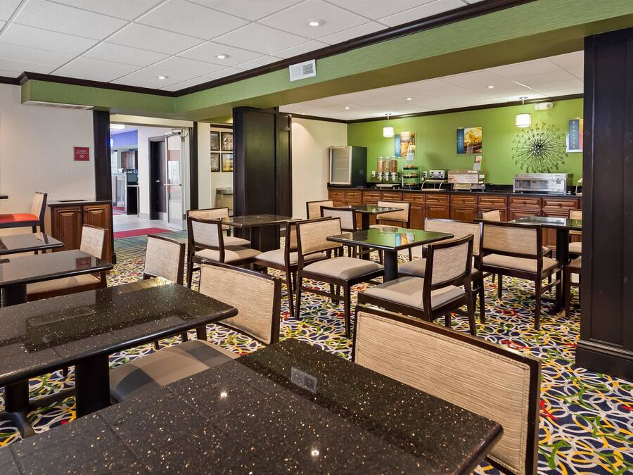 A hotel lobby with a dining area featuring tables and chairs, a kitchen area with appliances, and a green wall with various signs.