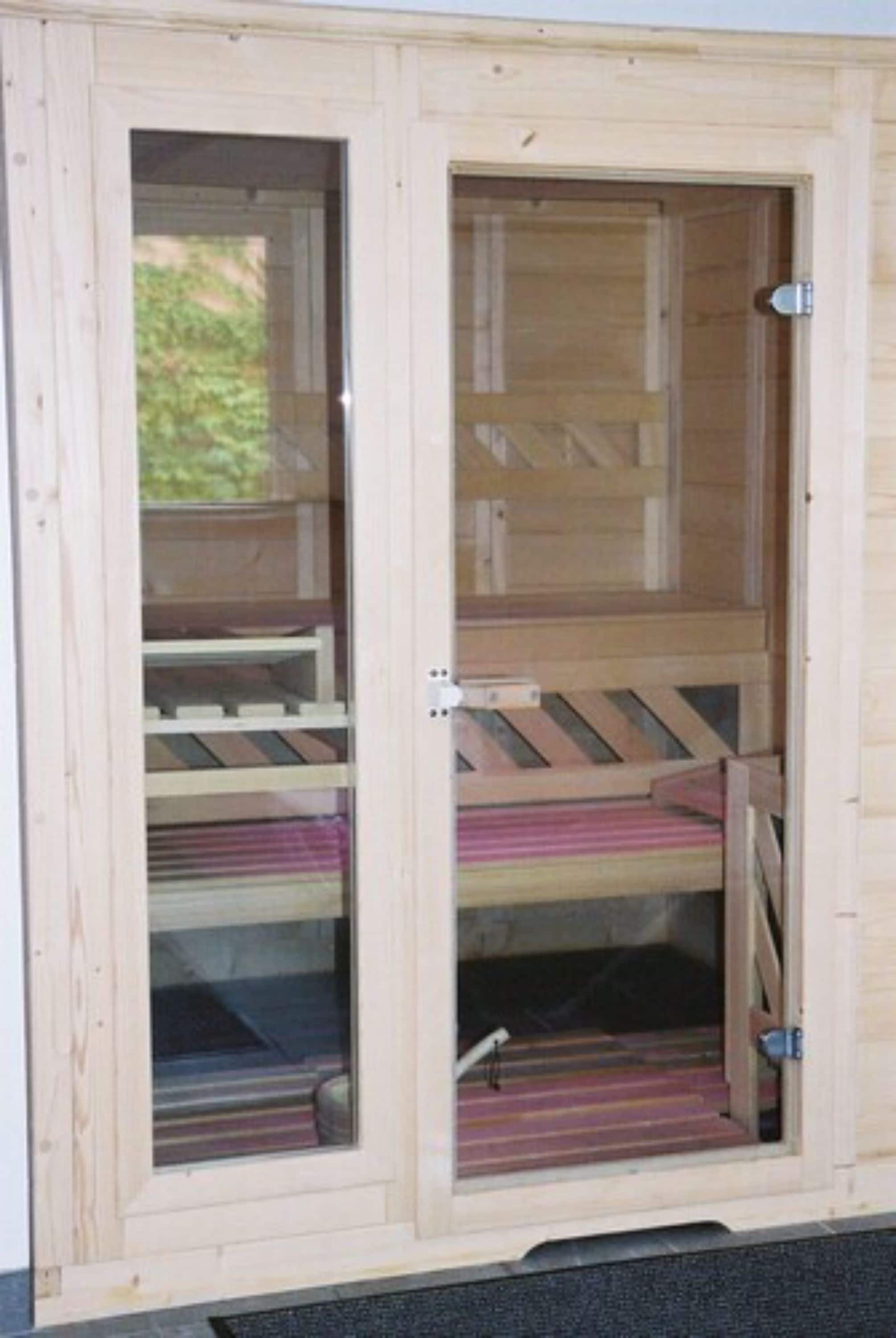A wooden structure with a glass door, a metal latch, and a wooden bench inside.