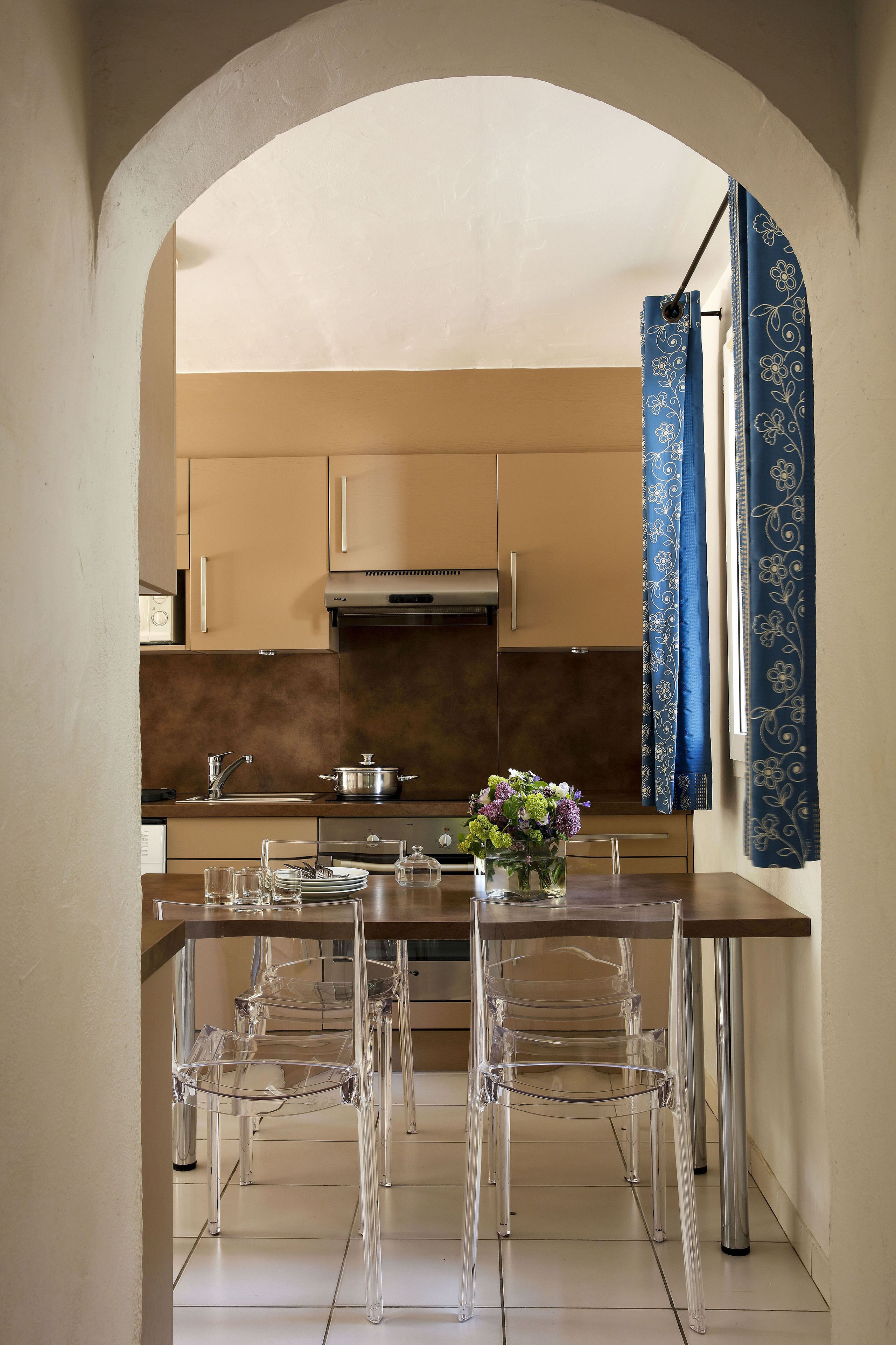 A modern kitchen with a central island, clear chairs, and a vase of flowers.