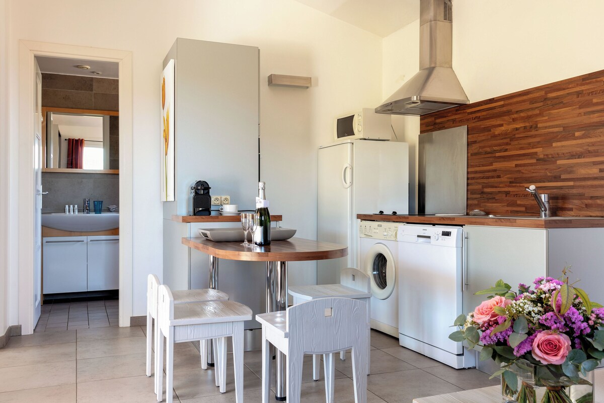 A modern kitchen with a built-in washing machine, a dining area with two chairs, and a wooden accent wall.