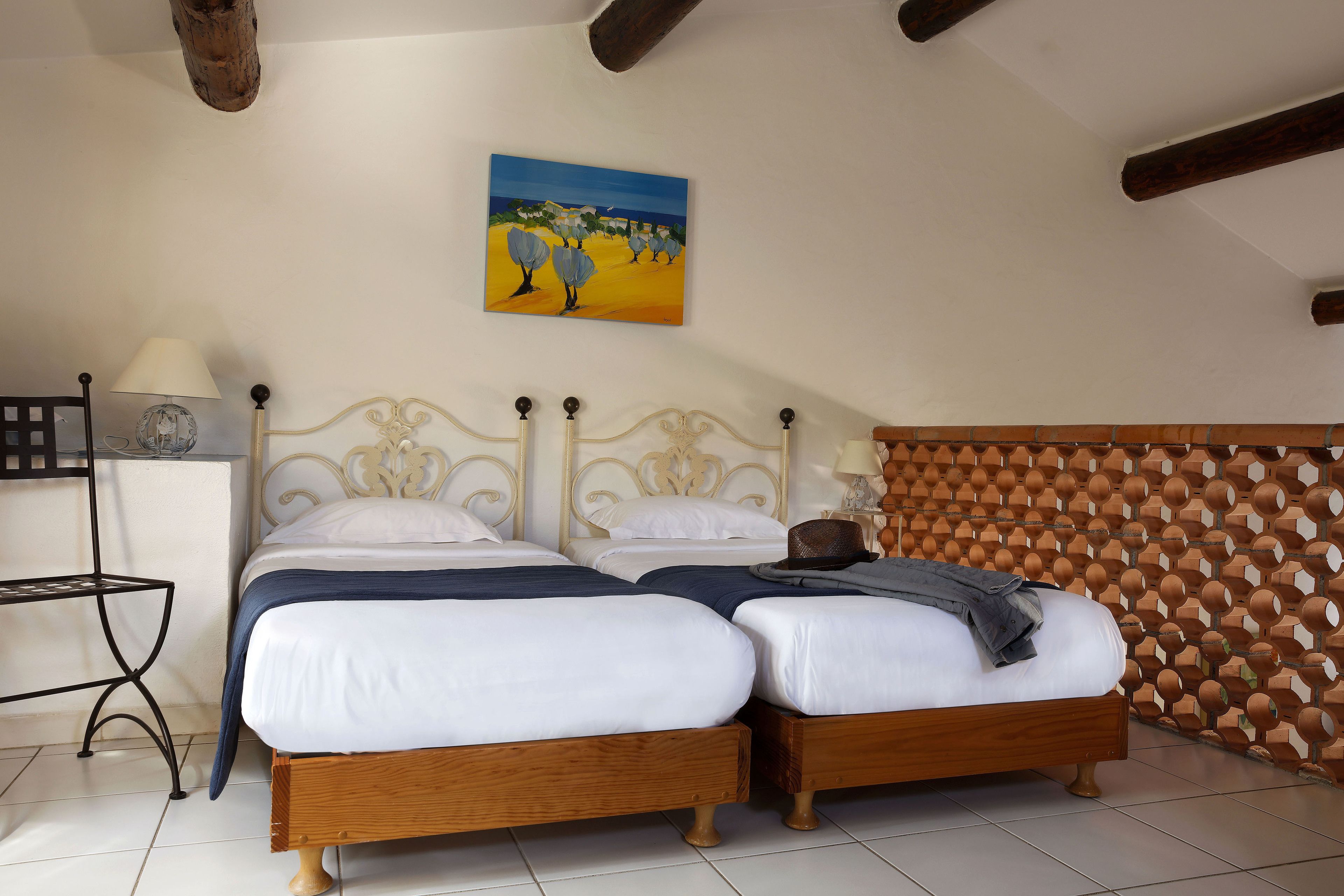 Una habitación con dos camas, un cuadro en la pared, una lámpara y un separador de madera.