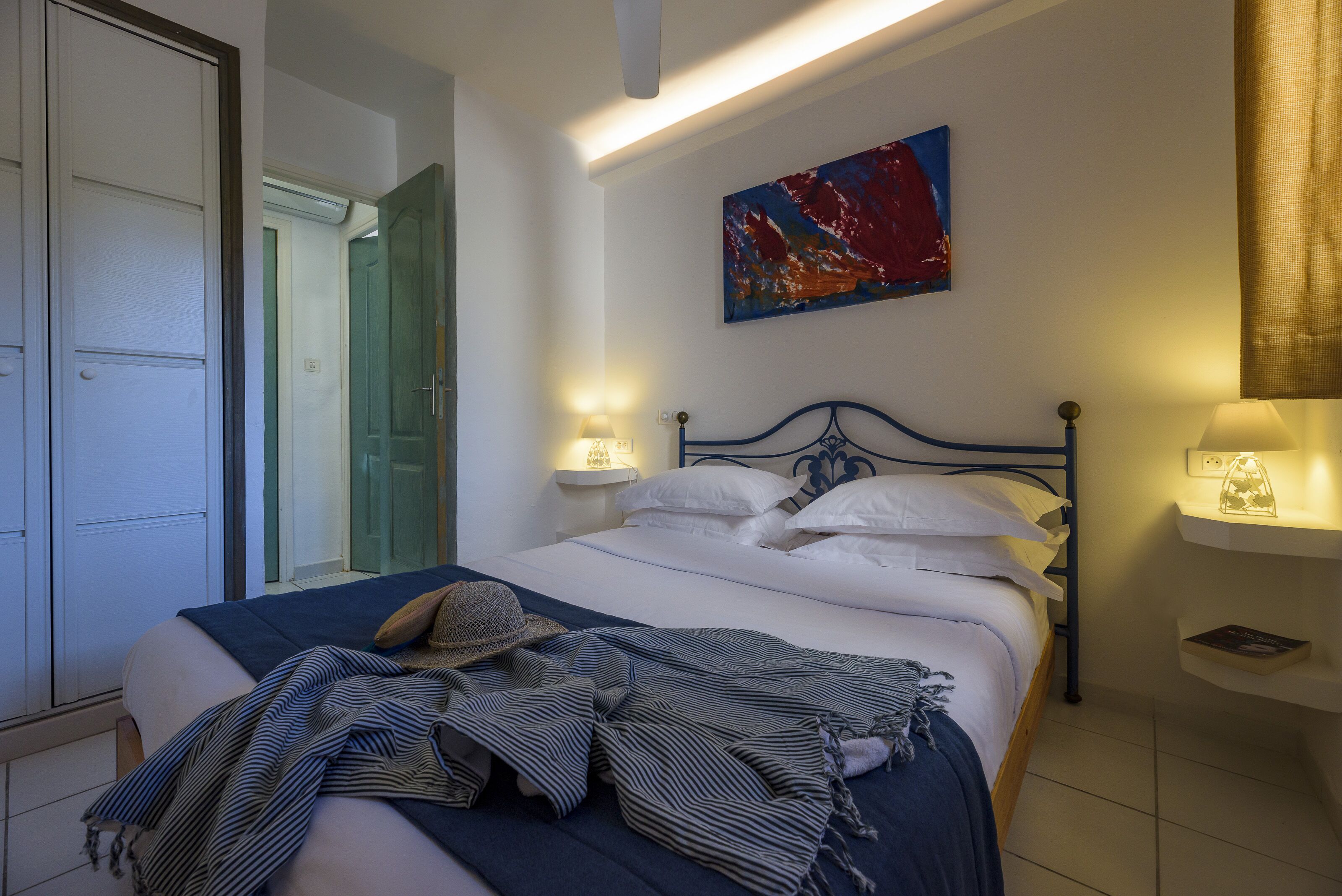 A bedroom with a bed, bedside lamps, a painting, and a door.