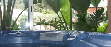 A hot tub with a blue textured surface, surrounded by large green plants and a metal railing.