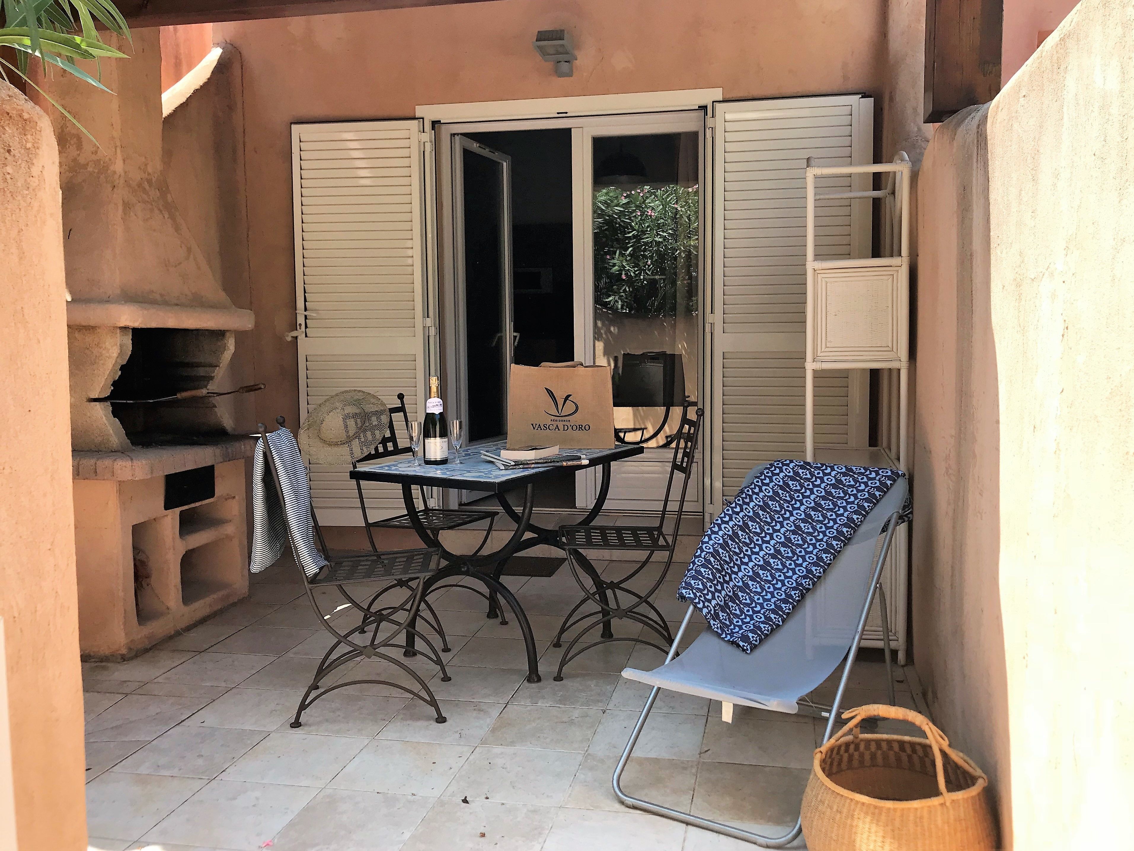 Un patio exterior con una mesa, sillas, una parrilla y una silla plegable.