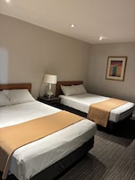 Habitación de hotel con dos camas, una mesita de noche con lámpara y un cuadro en la pared.
