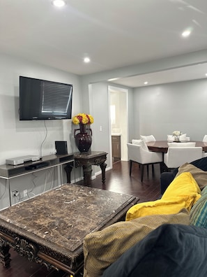 Una sala de estar moderna con un televisor de pantalla plana, una mesa de centro, un sofá y un comedor con sillas.