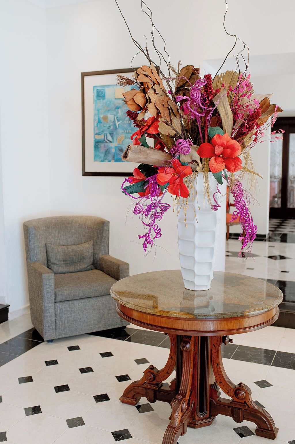 A round wooden table with a white vase containing dried flowers and greenery.