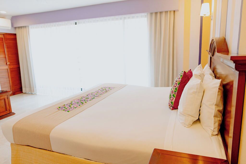 A hotel room with a large bed, a wooden headboard, and a window with curtains.