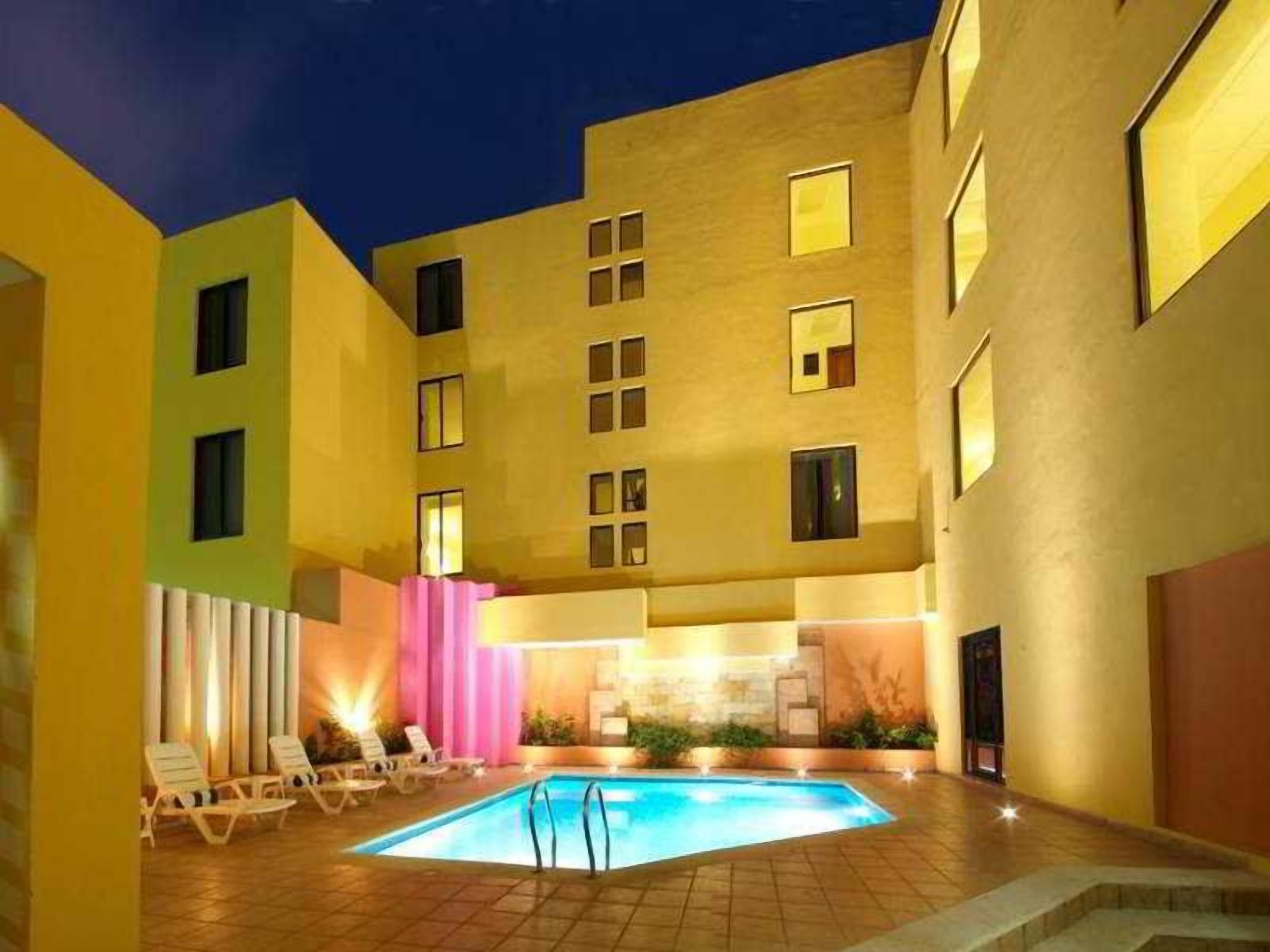 Un área de piscina con sillones de descanso y un edificio con varias ventanas.