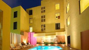 Un área de piscina con sillones de descanso y un edificio con varias ventanas.