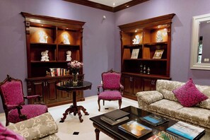 Una habitación con una mesa redonda, dos sillones, un sofá y estanterías empotradas decoradas con objetos ornamentales.
