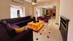 A spacious living area with a large sofa, a coffee table, and a chandelier. There is a bar area visible in the background. - Hotel Plaza Colonial (Campeche)