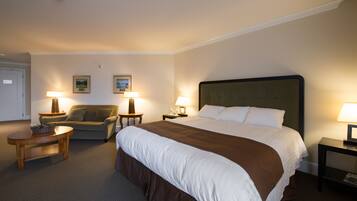 A hotel room with a large bed, two bedside tables with lamps, a sofa, and a small table with a basket.