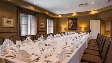 A long dining table set for a formal event with multiple chairs, candles, and a framed picture on the wall.