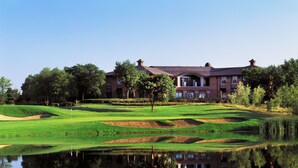 A golf course with a pond reflecting the surroundings, a brick building with multiple windows, and trees around the area. - The Glen Club (Glenview)