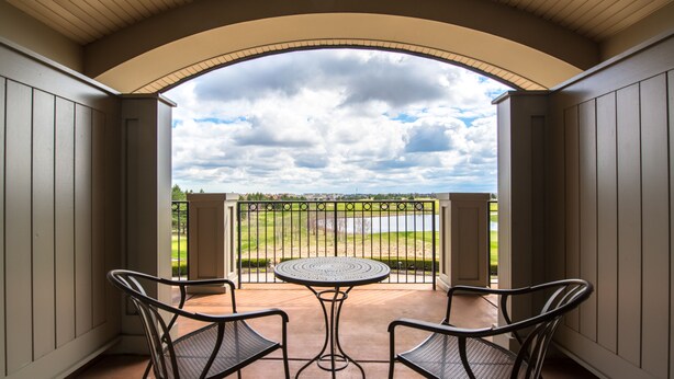 A balcony with a round table and two chairs, a view of a lake, and a cloudy sky. - The Glen Club (Glenview)