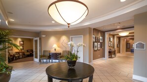 A spacious lobby with a round table, chairs, a potted plant, and a chandelier. - The Glen Club (Glenview)