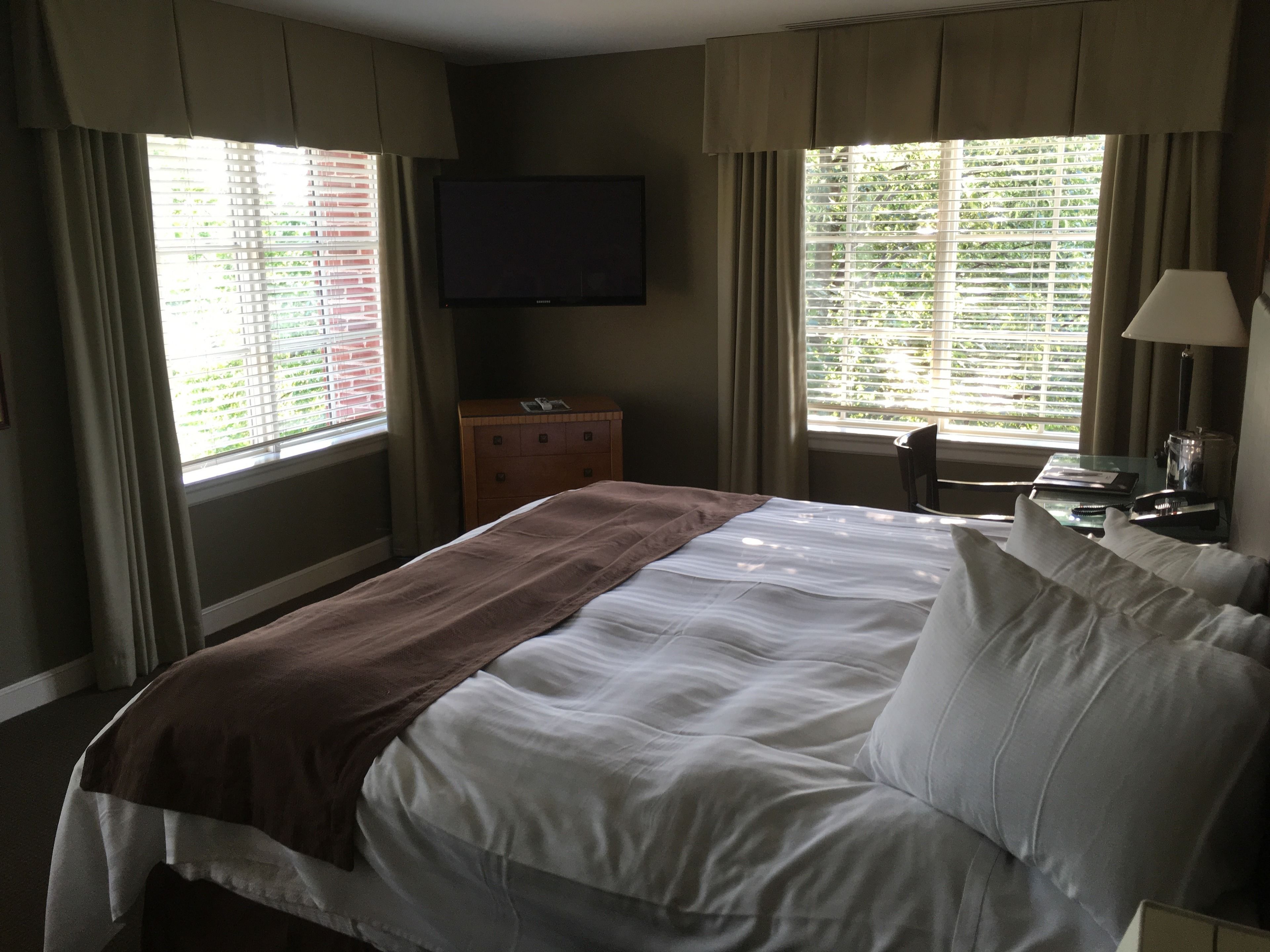 A hotel room with a bed, a TV, a dresser, and a window with blinds.